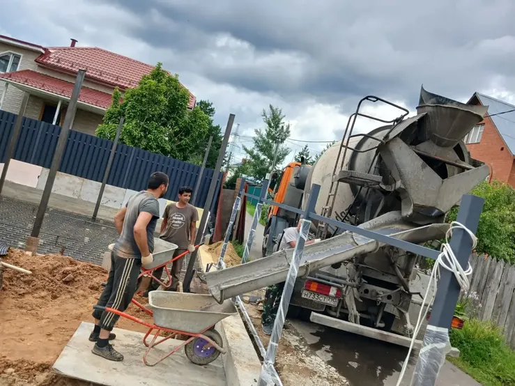 Рабочие принимают бетон из миксера через лоток на частной стройке