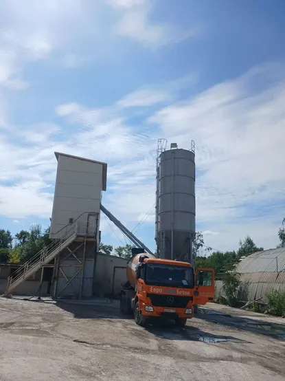 Миксер у здания бетонного завода с силосами